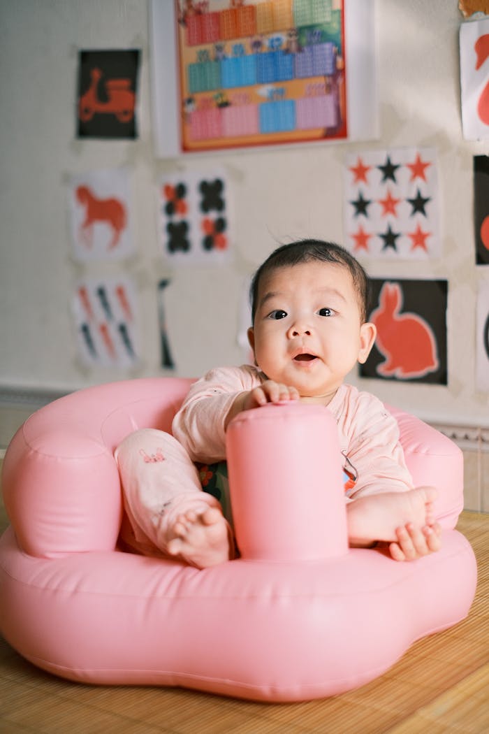 Cute baby sitting in a pink inflatable chair surrounded by colorful wall decorations indoors.